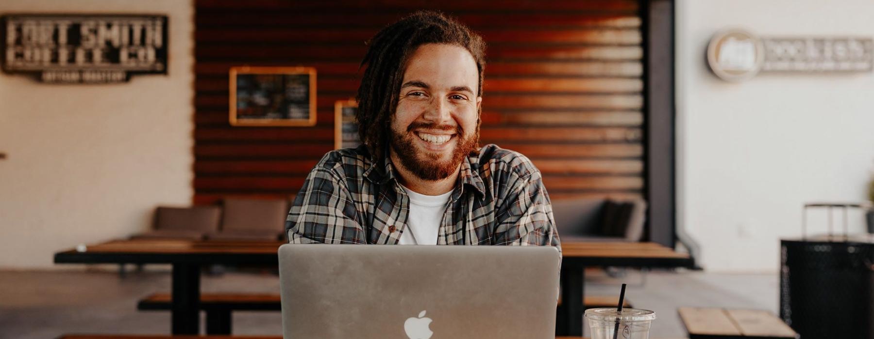 man sits with a drink in front of an open laptop in local restaurant
